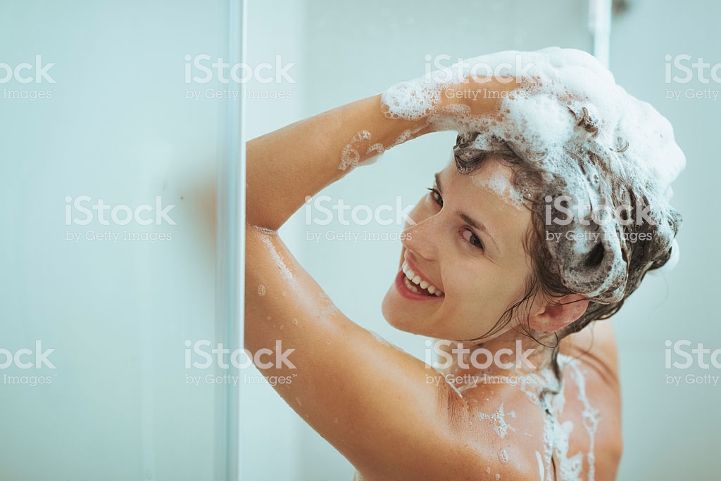 Smiling young woman washing head with shampoo